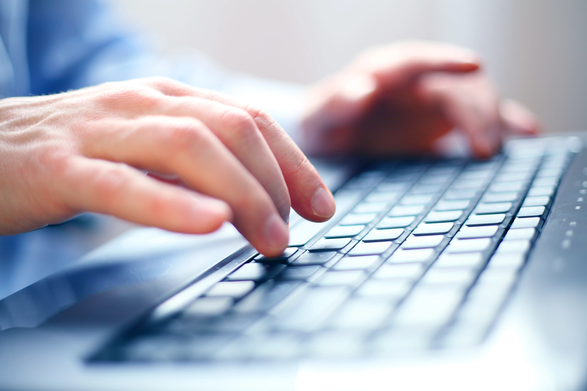 Eine Nahaufnahme der Hände eines Mannes, die auf einer Laptop-Tastatur tippen.