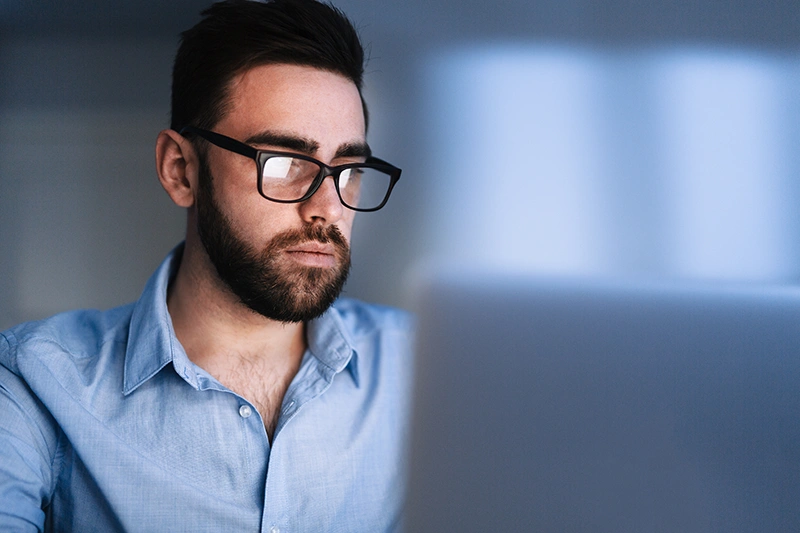 Ein Mann mit Brille und kurzem Bart sitzt konzentriert hinter einem Laptop und arbeitet.